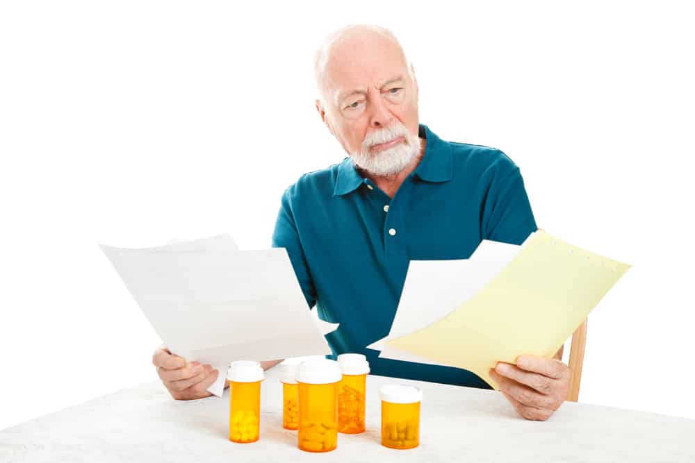 Senior man depressed by a pile of medical bills.  Isolated on white.