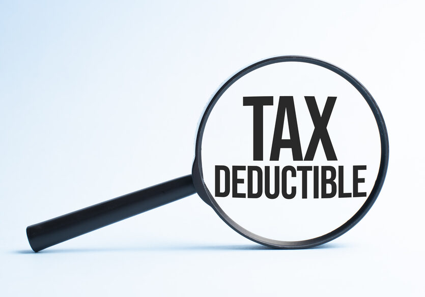 Magnifying glass with the word TAX DEDUCTIBLE. Business concept